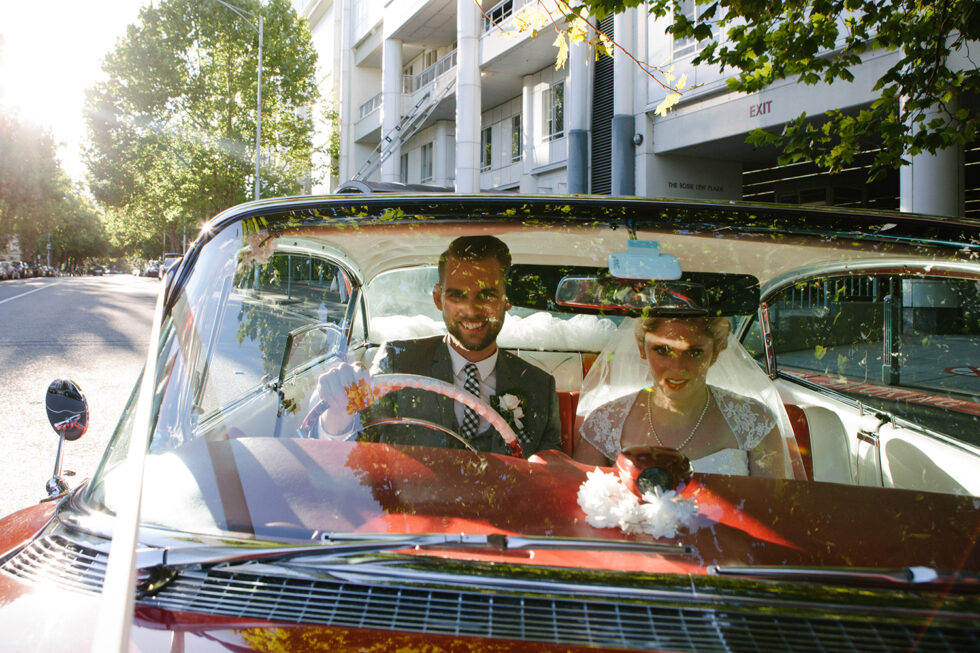 the married couple driving a red vintage car