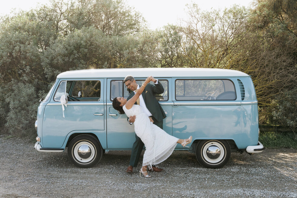 A couple is dancing in front of a blue vintage minivan.