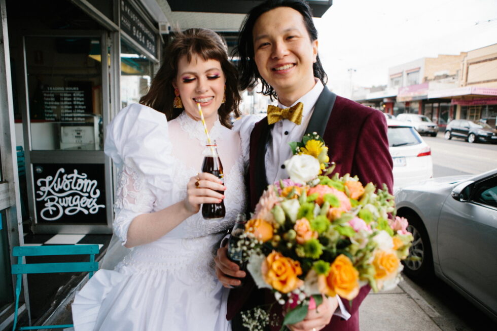 newly-married couple strolling down the street, sipping Coca Cola and holding a bouquet