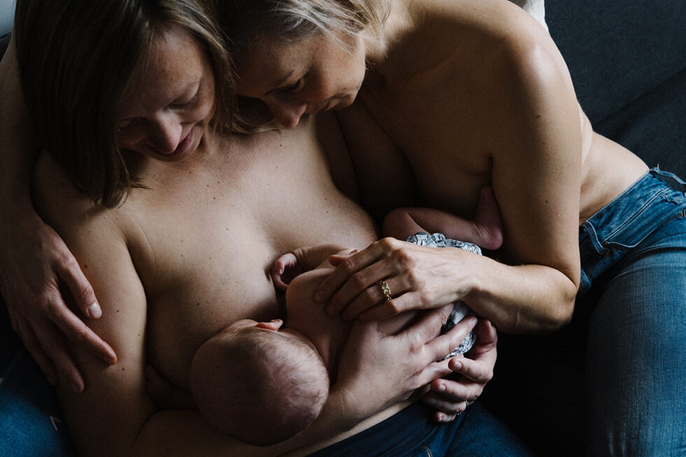 A couple is feeding their newborn baby while holding them close in a skin-to-skin position.