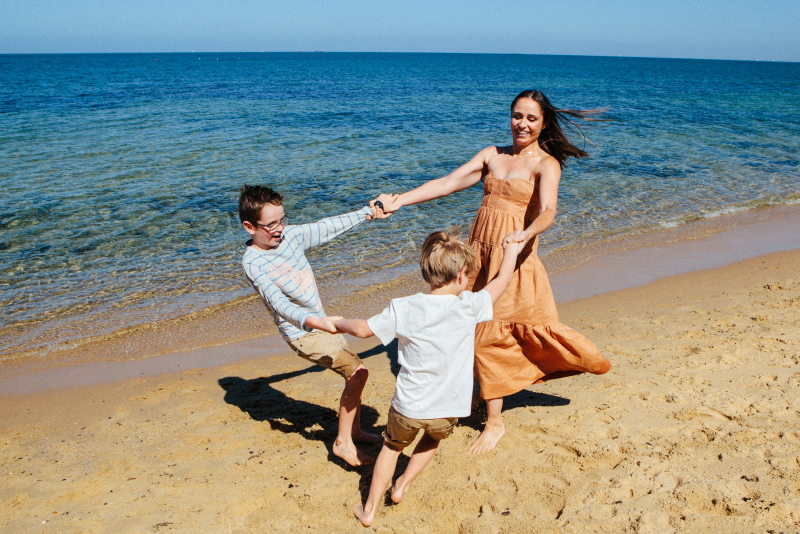 A mom and her kids dancing in a circle at the beach.