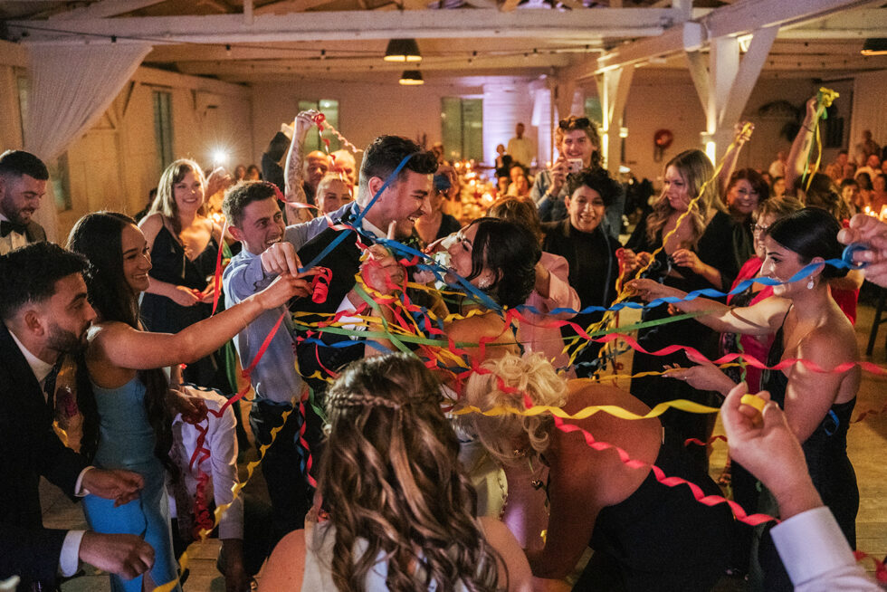 Bride and groom are in the middle of the guest crowd, throwing paper twists