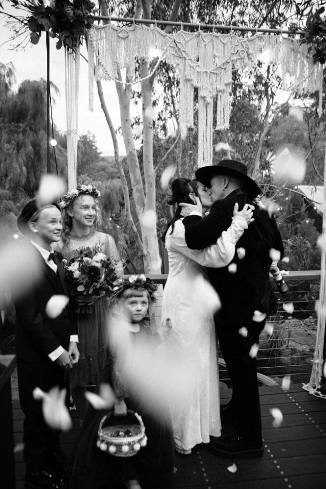 Bride and groom kissing under a shower of white rose petals