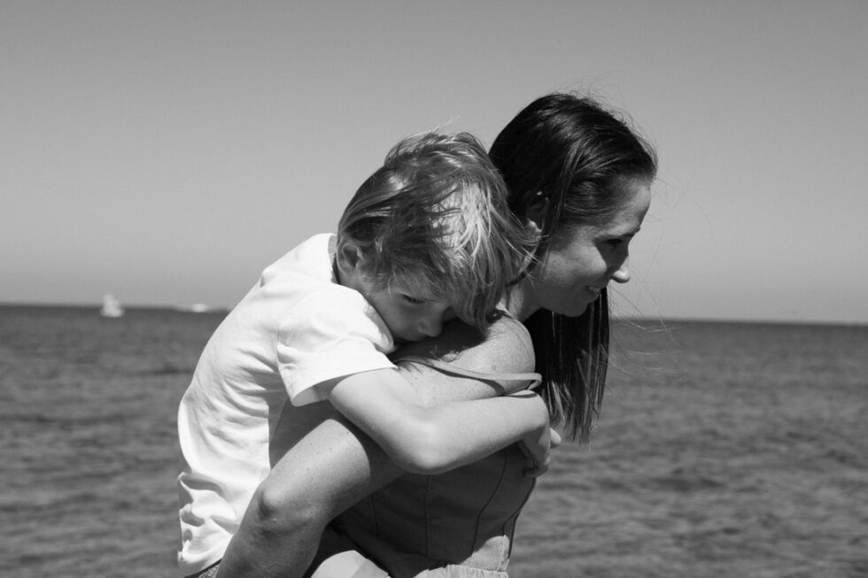 Mom is walking on the beach with her son on her back