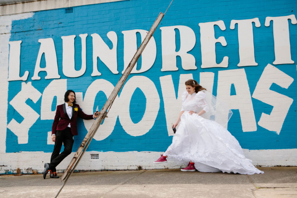 The bride and groom are posing in front of an old sign on the street in Thornbury Melbourne North